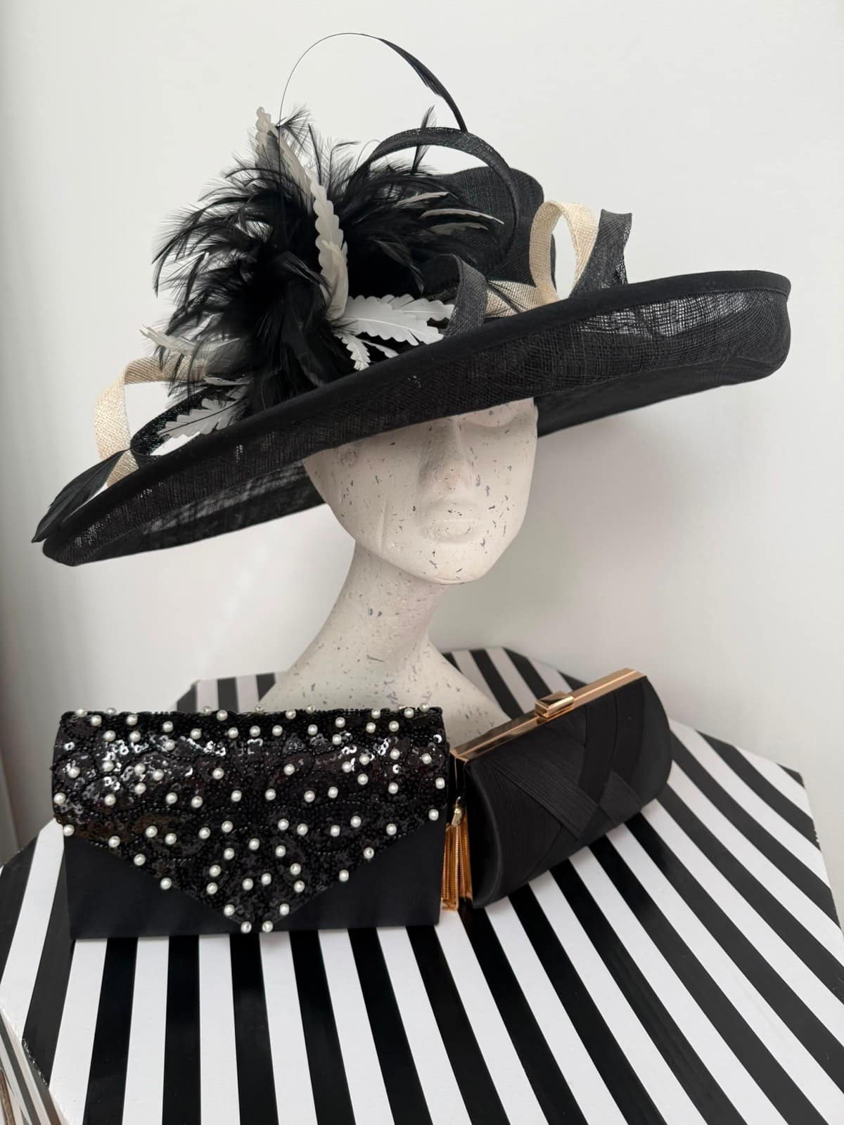 Black and ivory wide-brim occasion hat with a dramatic feather spray and cream sinamay loops, with two black clutches