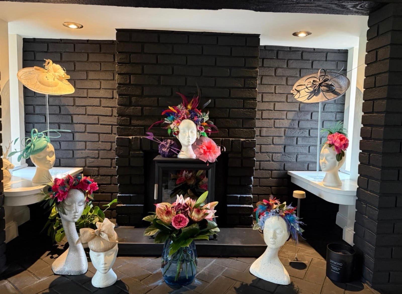 The Hatisserie showroom — occasion hats and fascinators displayed on mannequin heads around a dark brick fireplace