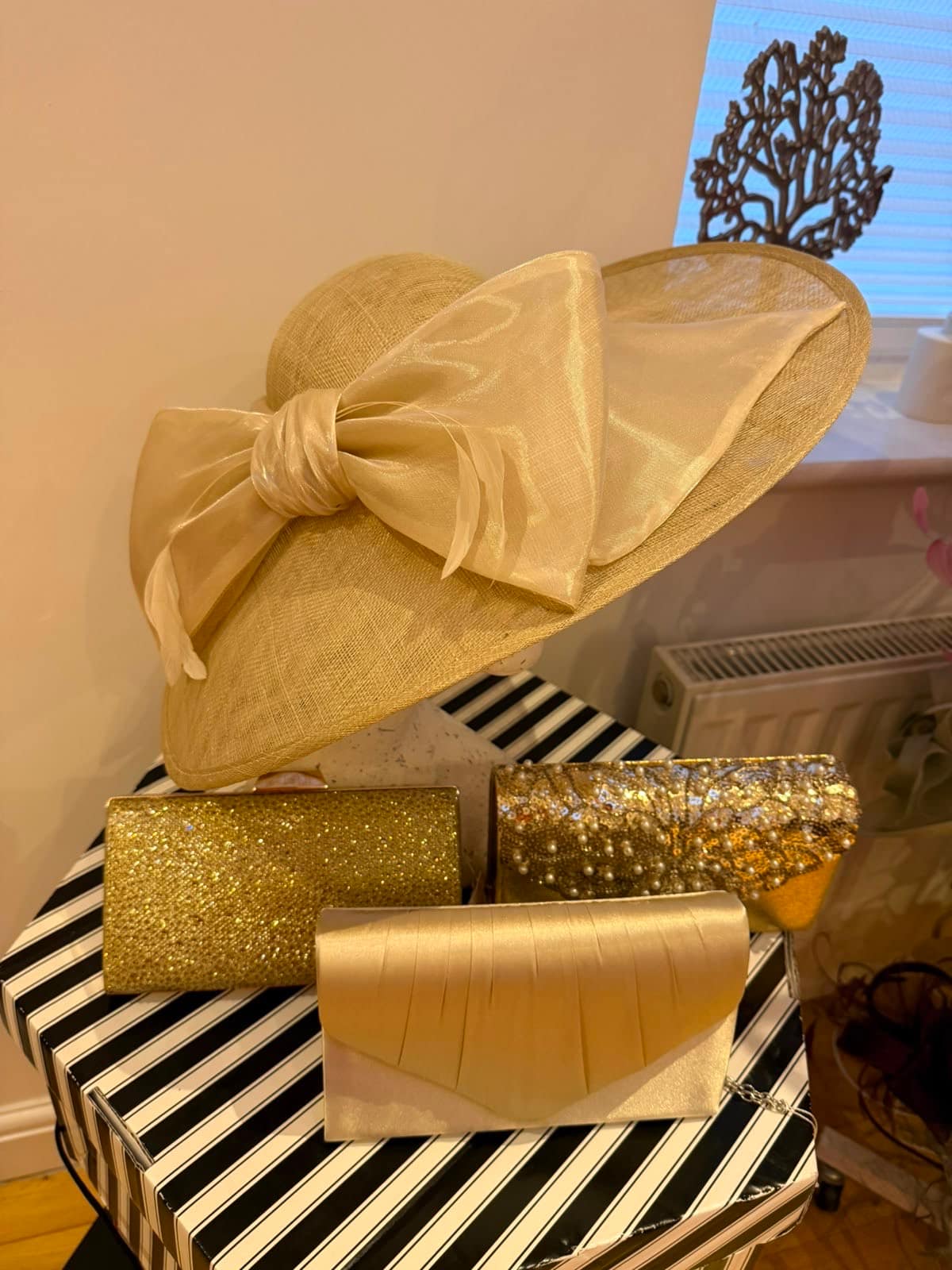 Blush champagne teardrop hatinator with satin roses and feathers, shown with beaded gold and satin clutch bags